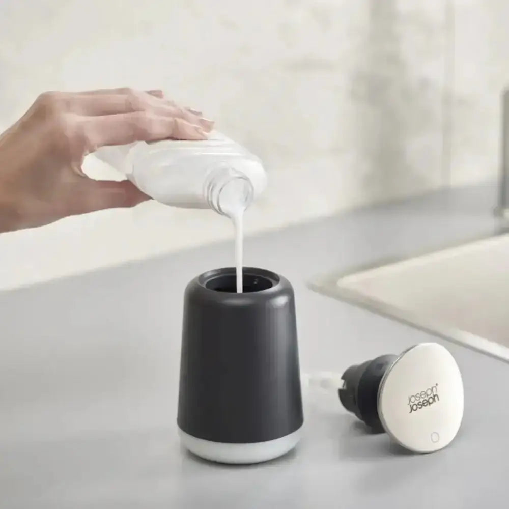 Hand pouring soap into a black and white dispenser on a bathroom counter.