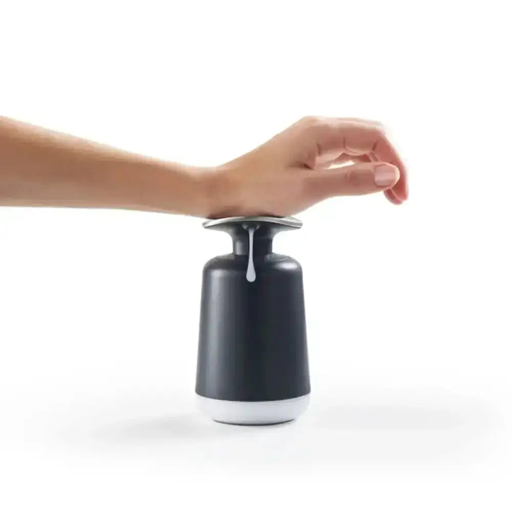 Hand pressing a black soap dispenser with soap dripping onto a white background
