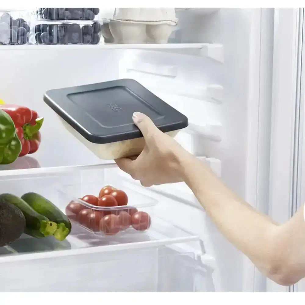 Hand placing a container into an open refrigerator with vegetables inside.
