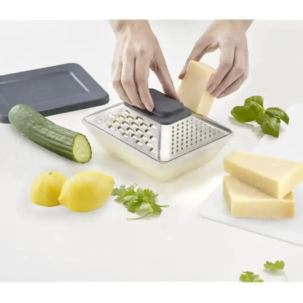Person using a box grater with vegetables and cheese on a white surface