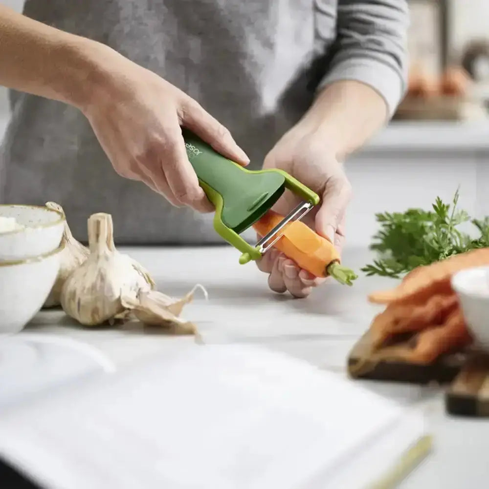 Person using a green vegetable peeler on a carrot on a kitchen counter.