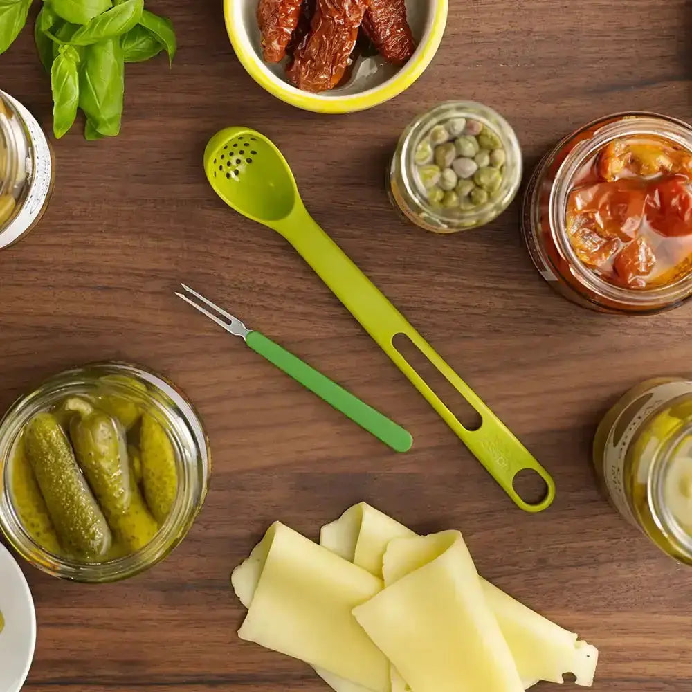 Wooden table with jars of pickles, cheese, and a green ladle.