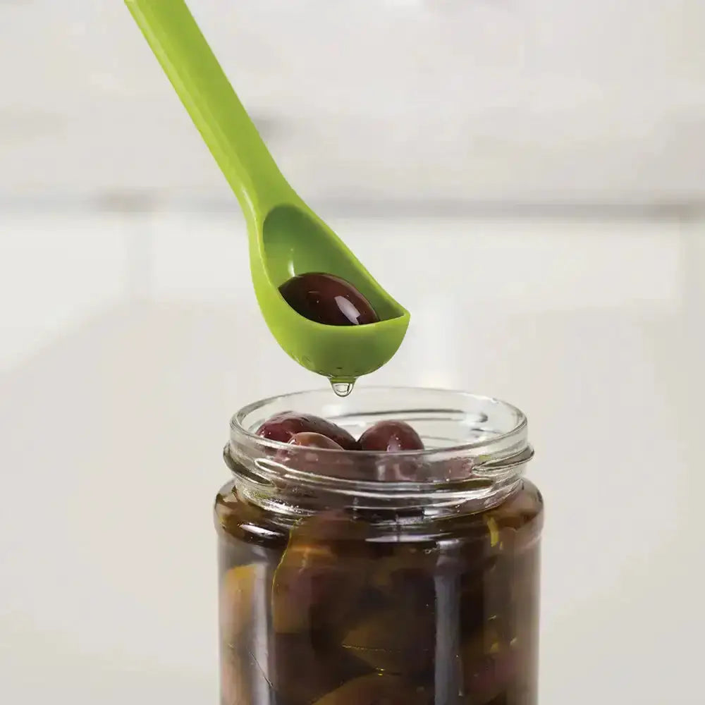 Green spoon lifting a small amount of olives from a jar on a white background