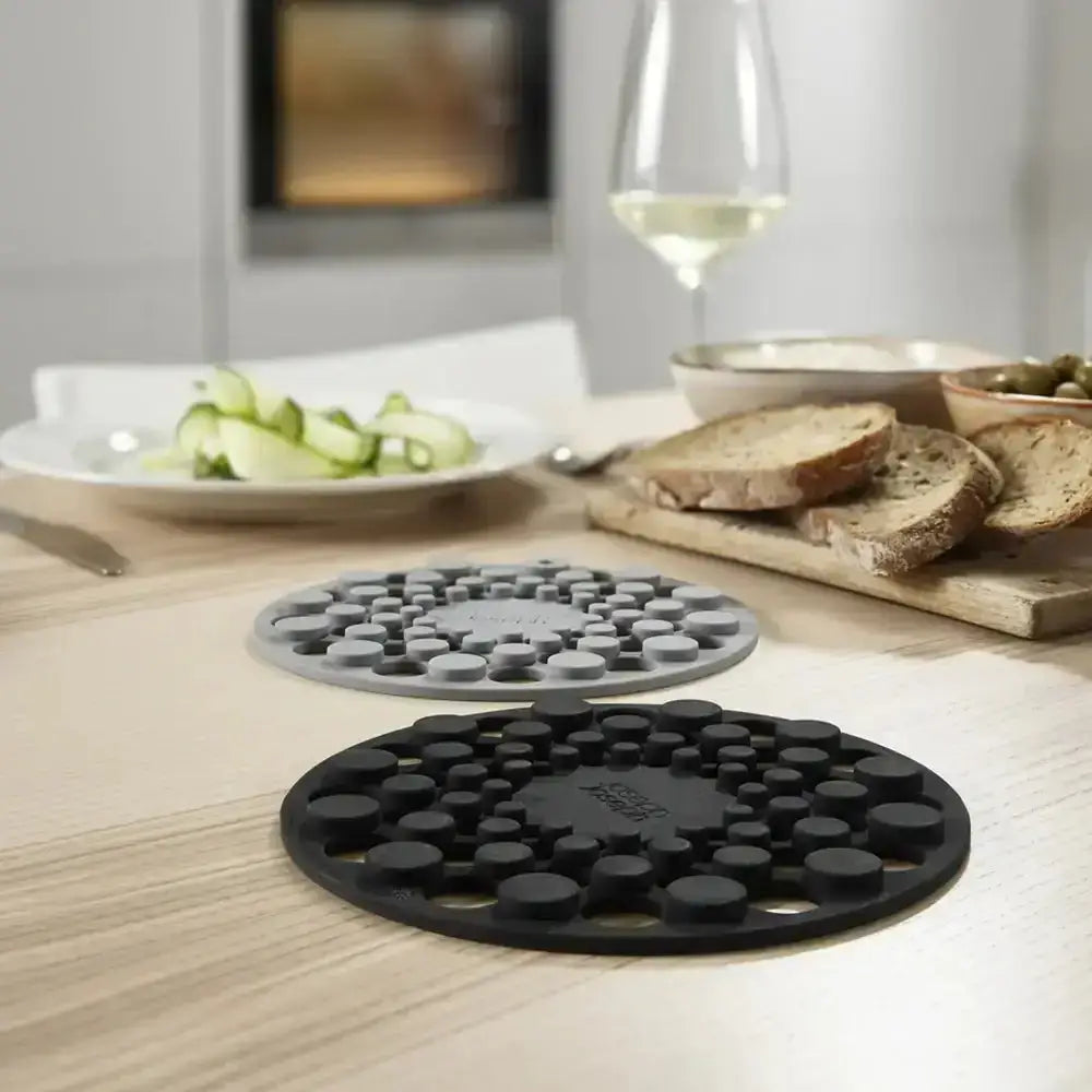 Two round silicone trivets, one gray and one black, on a wooden counter top