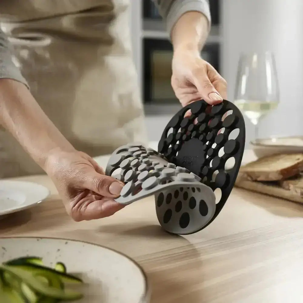 Person holding a black and gray kitchen tool on a wooden table with a blurred background