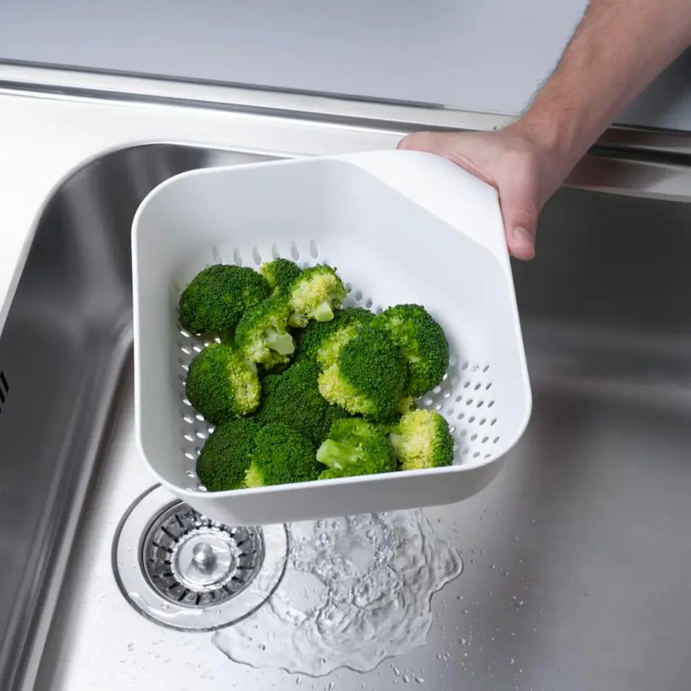 Person holding a white colander with broccoli over a sink