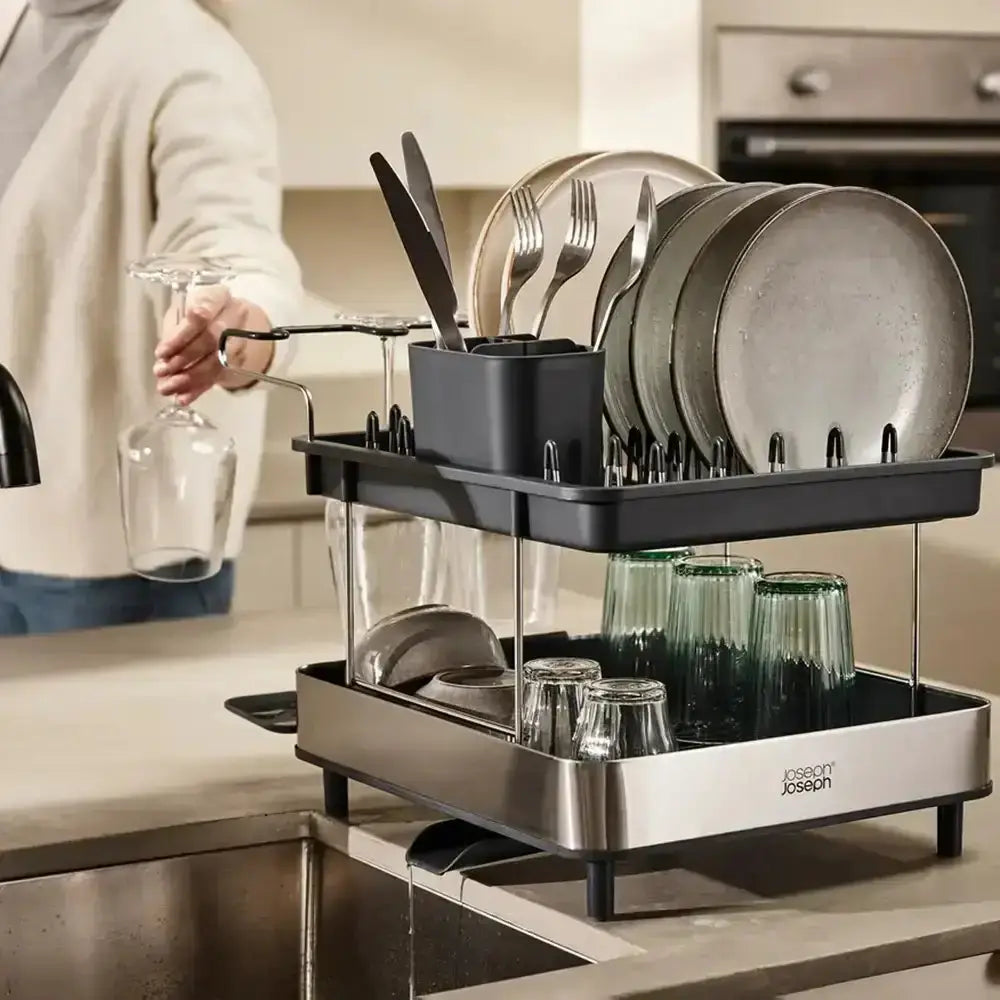 Dish drying rack with plates, glasses, and cutlery in a kitchen setting.