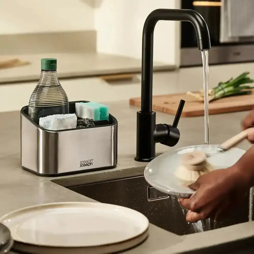 Person washing dishes in a kitchen with a black faucet and Joseph Joseph dish rack.