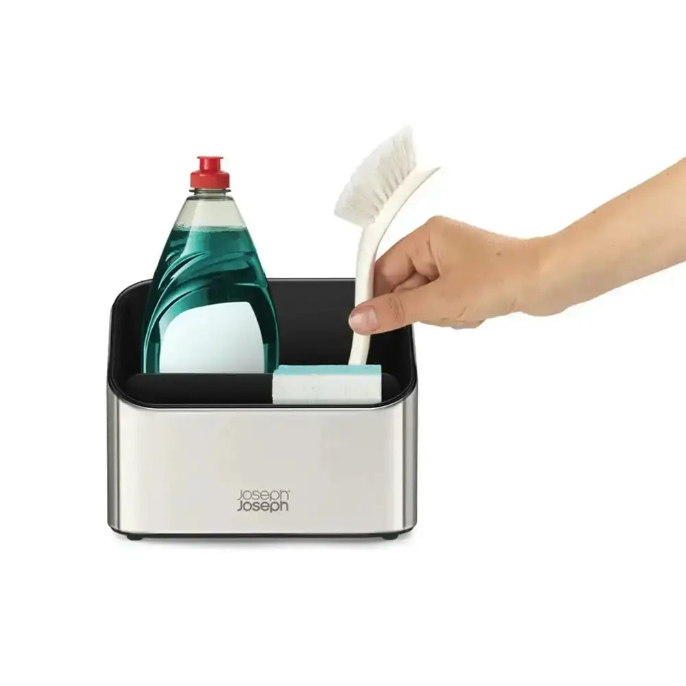 Hand reaching into a Joseph Joseph kitchen caddy with cleaning supplies on a white background