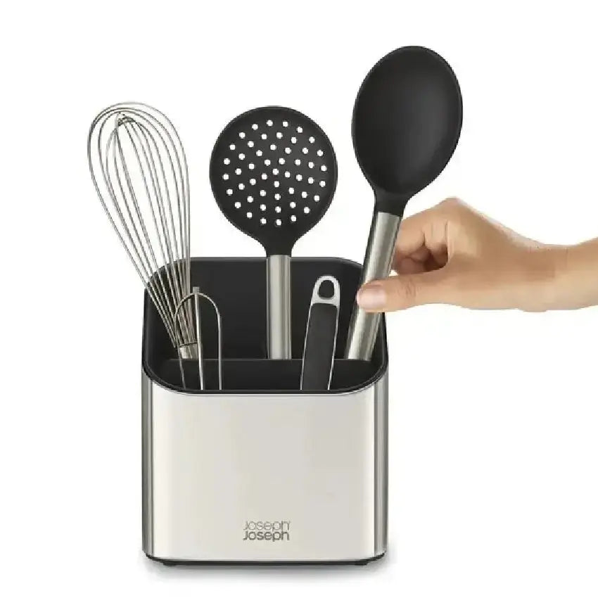 Kitchen utensils in a holder with a hand holding a spoon, on a white background.