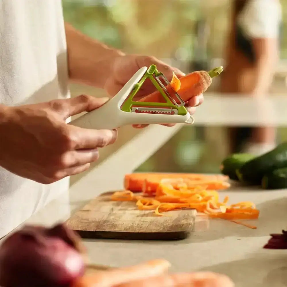 Person using a vegetable peeler to peel a carrot on a wooden cutting board.
