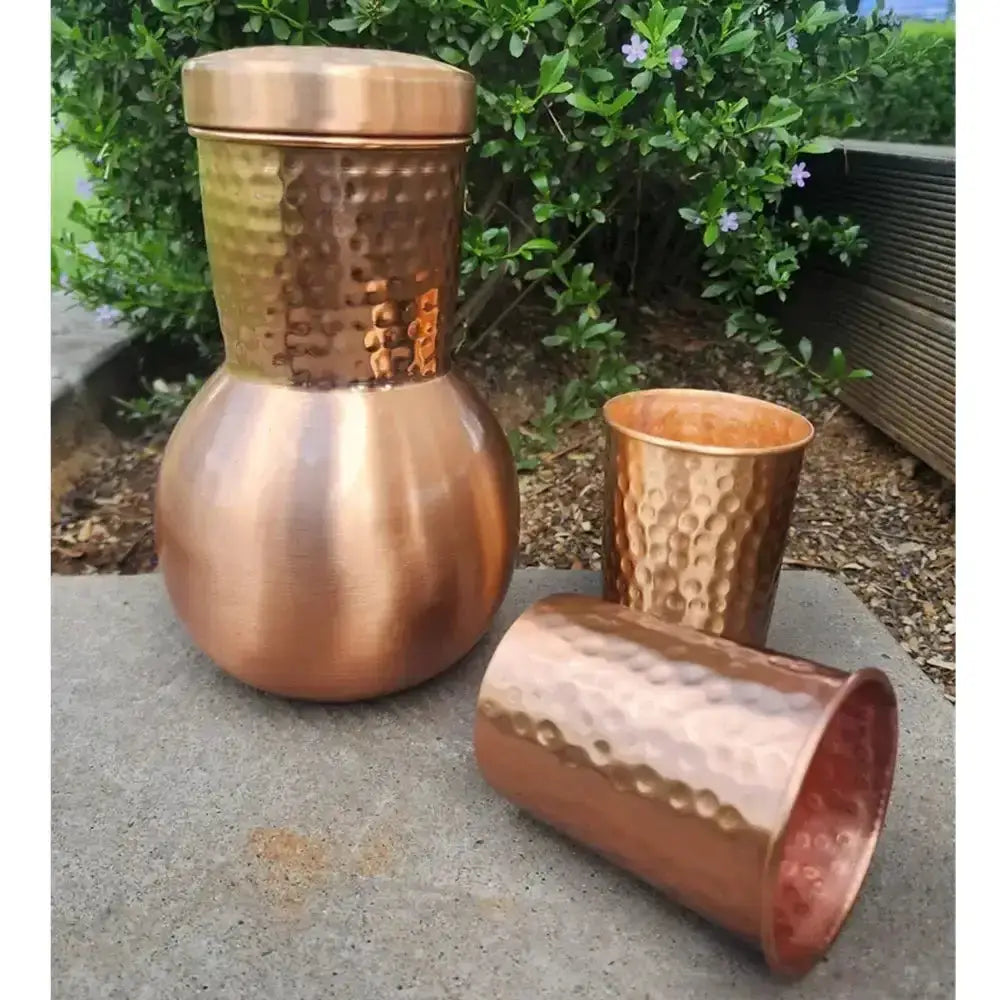 Set of copper tumblers on a concrete surface with greenery in the background