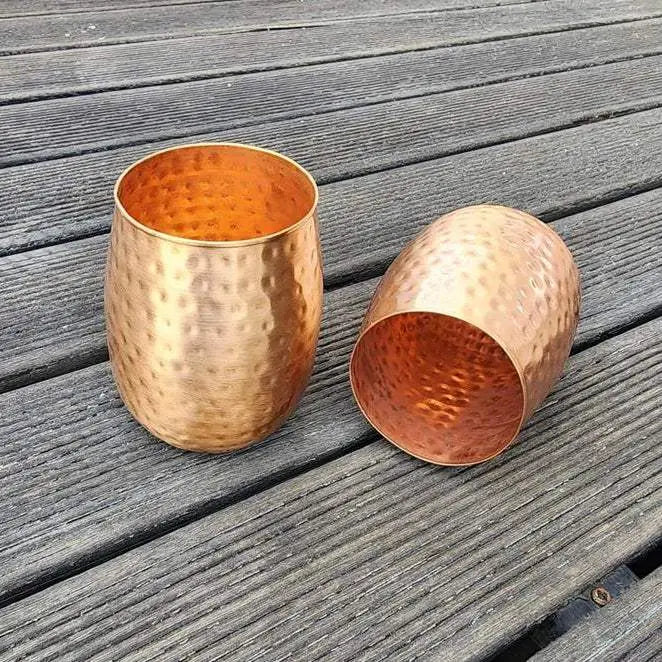 Two copper tumblers on a wooden surface