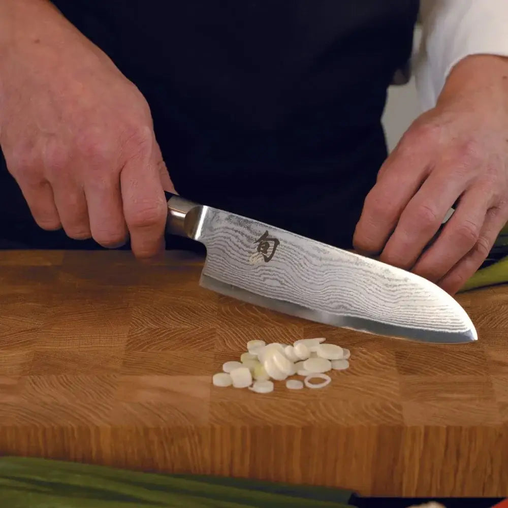 Person using a Shun knife to slice garlic on a wooden cutting board