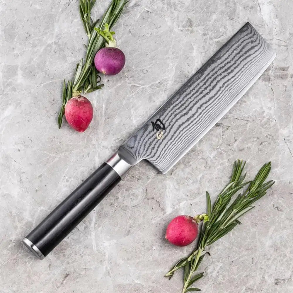 Chef's knife with a black handle on a gray surface with radishes and rosemary.