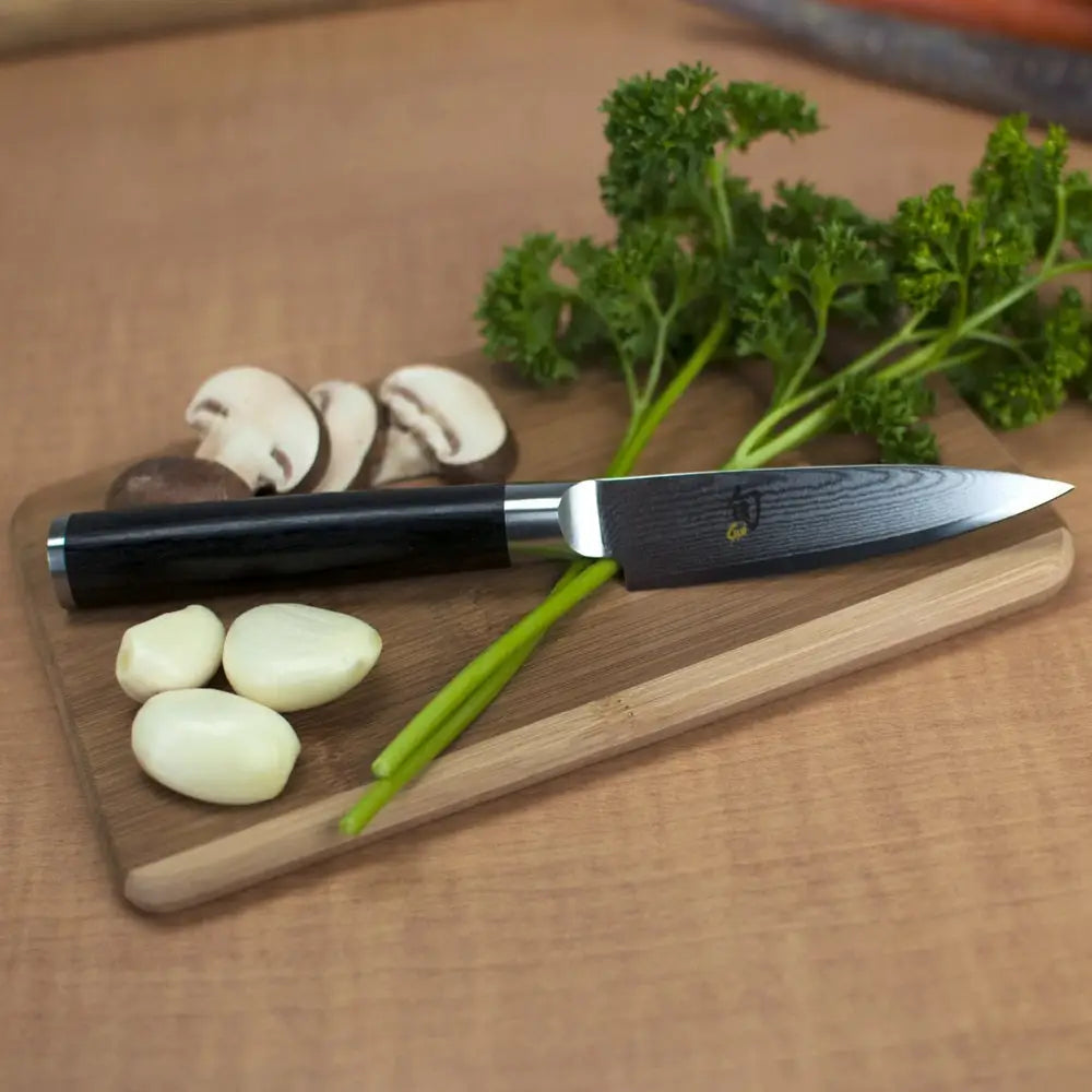 Kai shun classic paring knife with pakkawood handle and damascus steel blade resting on wooden cutting board