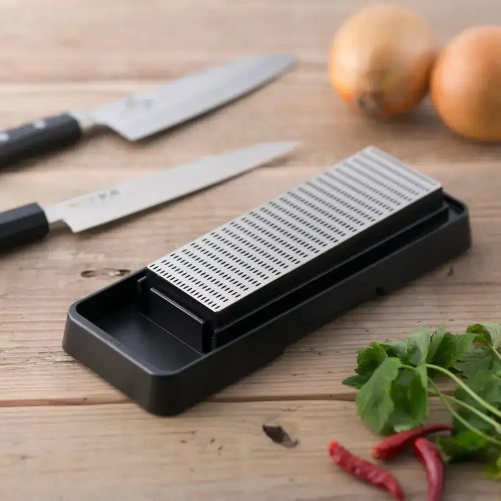 Knife sharpener on a wooden surface with knives and vegetables in the background