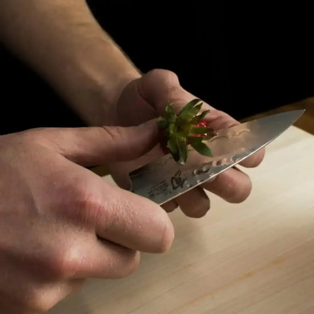 Person holding a strawberry and a knife on a wooden surface