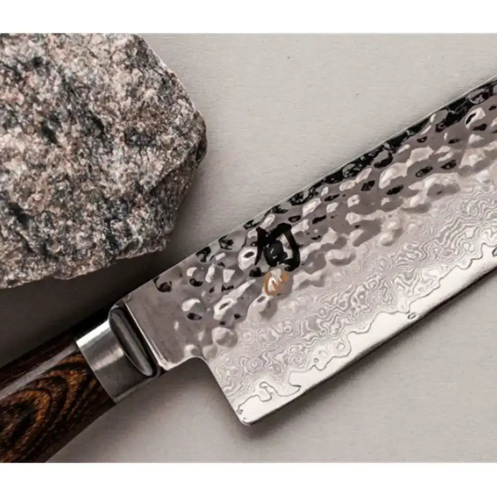 Knife with a decorative blade and wooden handle on a gray surface next to a rock.