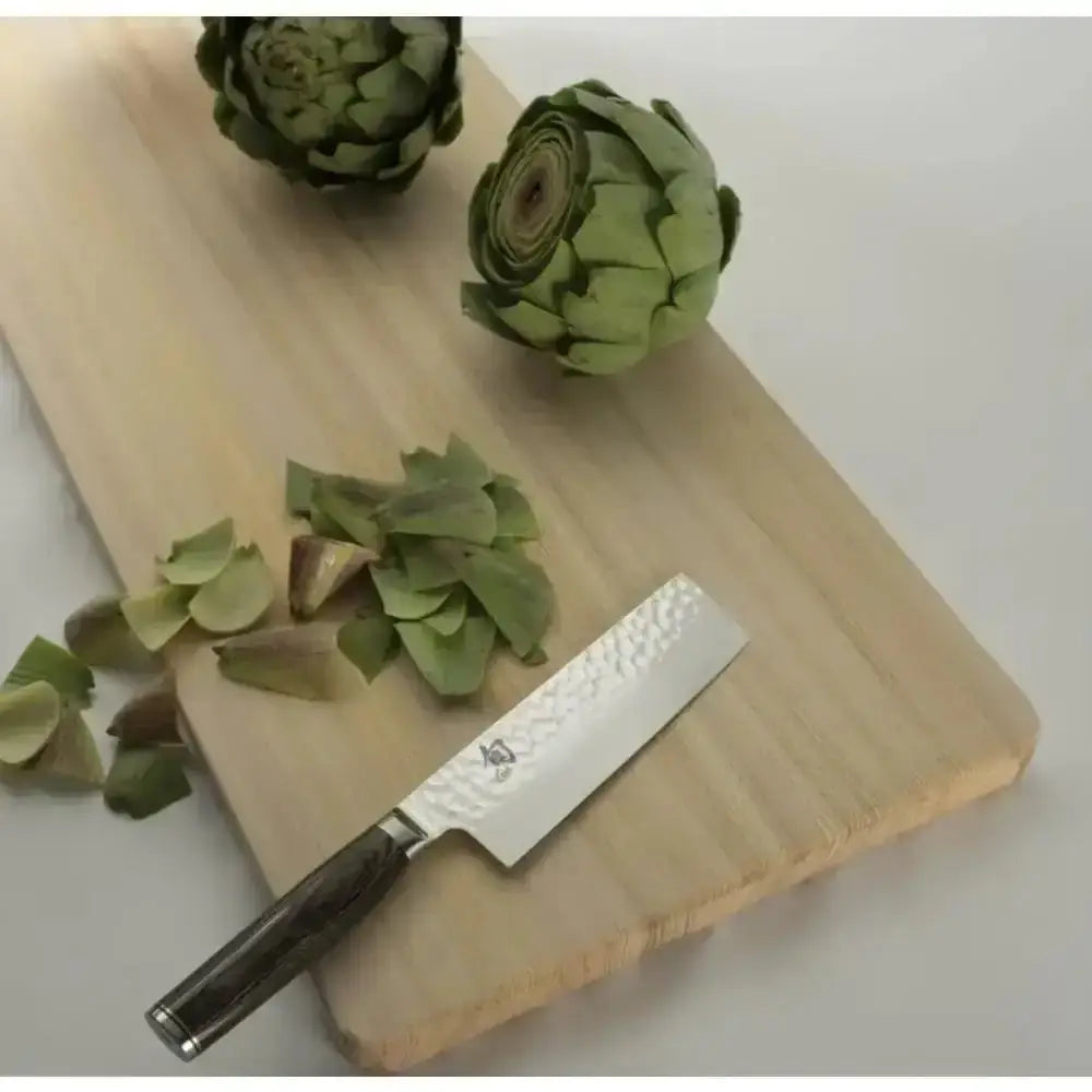 Knife on a wooden cutting board with artichokes and cut pieces