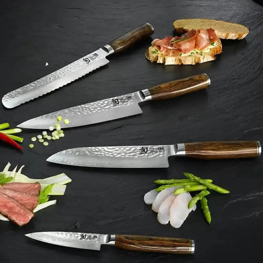 Set of kitchen knives with wooden handles on a dark surface with food items.