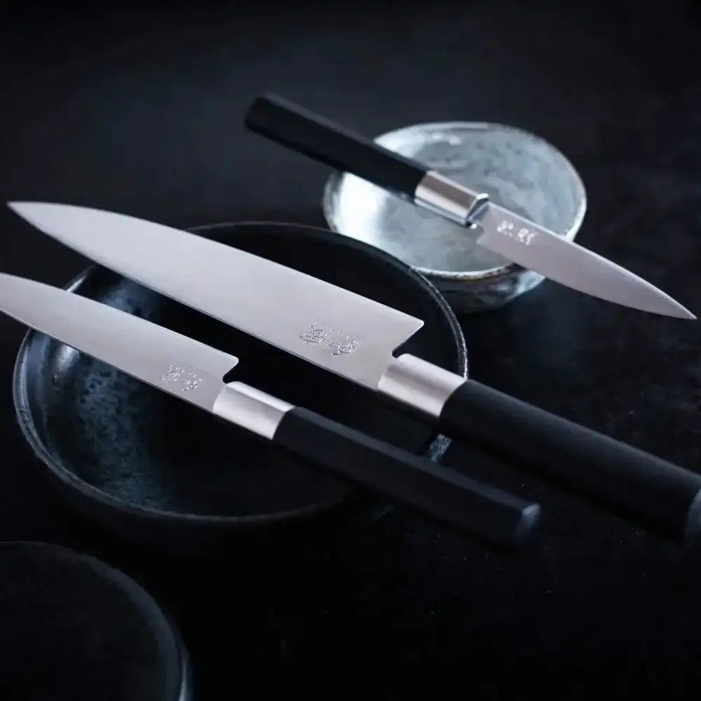 Three chef's knives with black handles on a dark surface