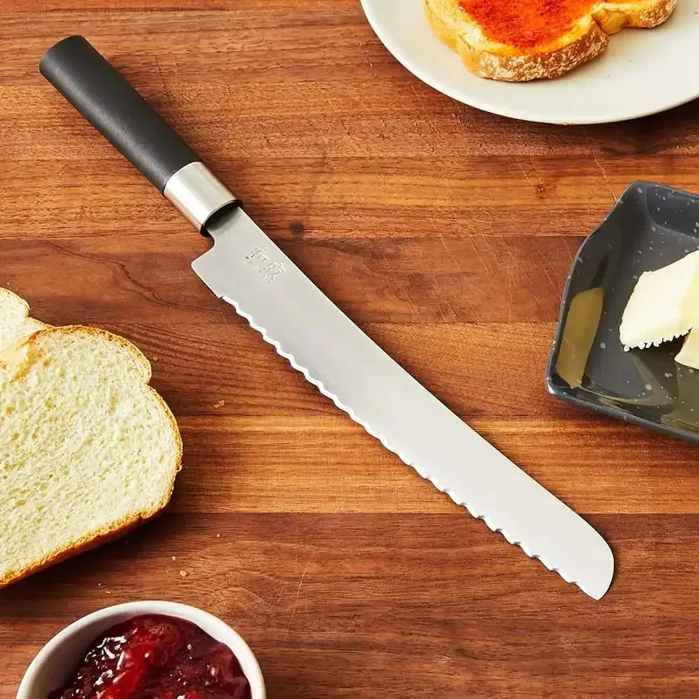 Bread knife on a wooden surface with bread, butter, and jam.