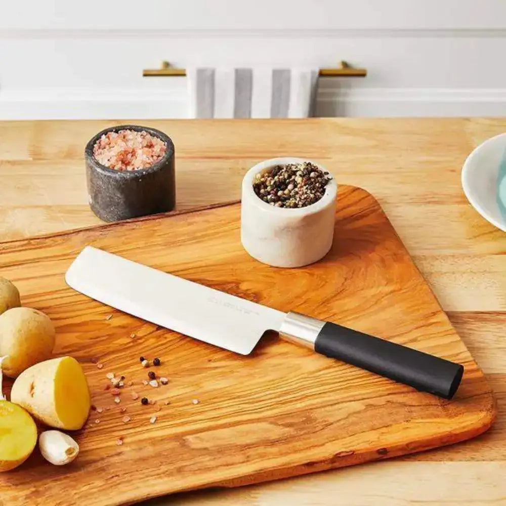 Wooden cutting board with a knife, potatoes, and spices on a kitchen counter.
