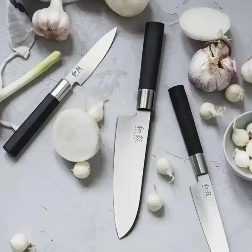 Set of knives with black handles on a gray surface with garlic and onions.