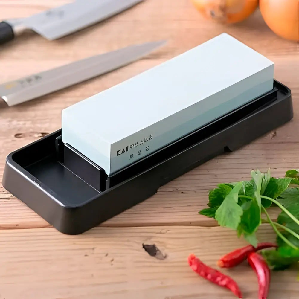 KAI brand whetstone on a black holder with a knife and vegetables on a wooden surface