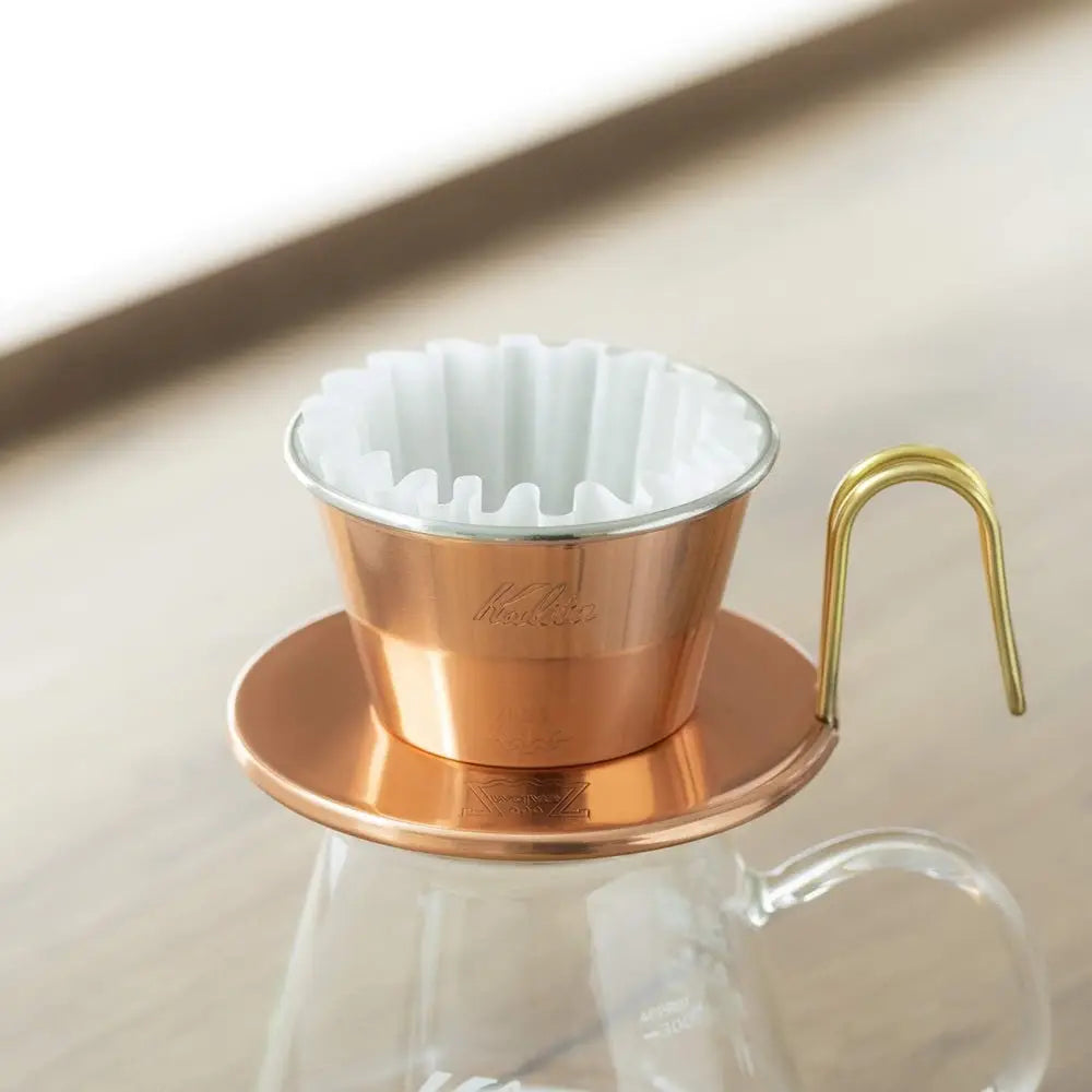Copper coffee dripper with white filter on a beige surface