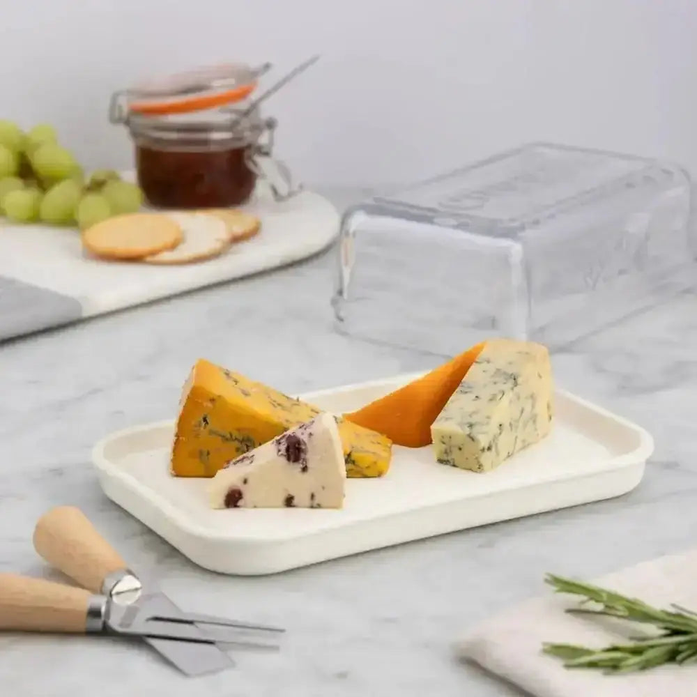 Assorted cheeses on a white plate with a cheese knife on a marble surface.