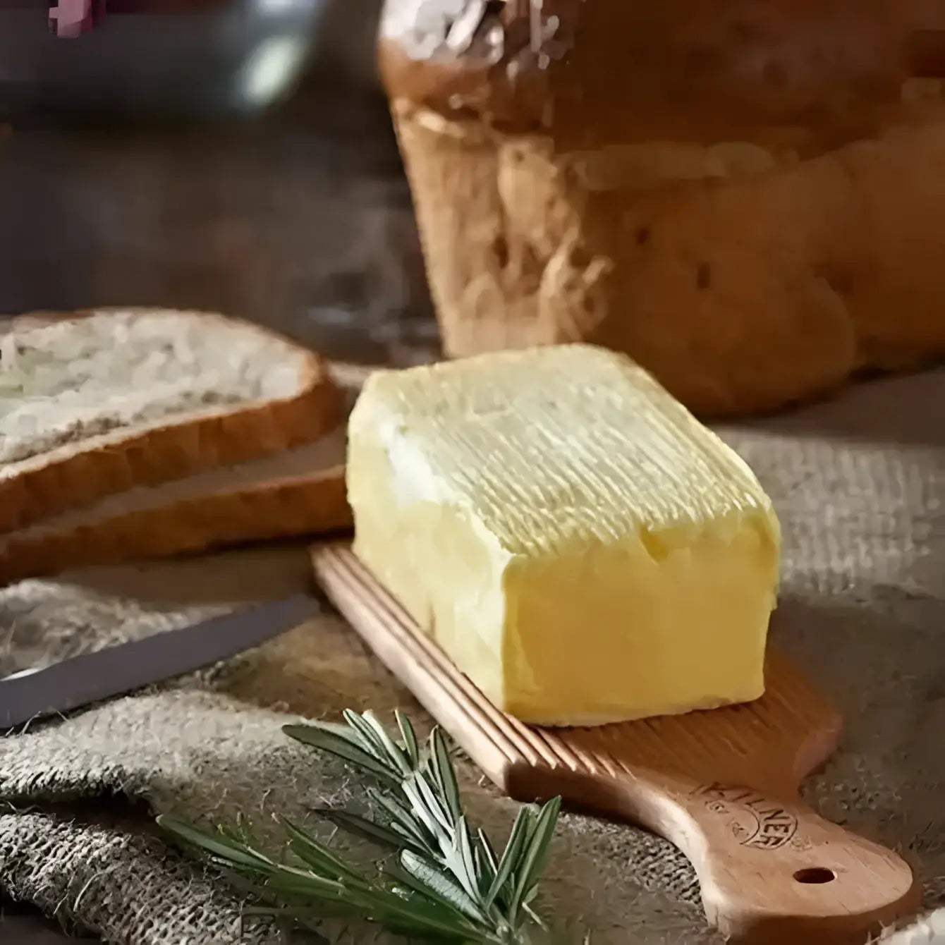 Block of butter on a wooden board with bread and a knife in the background