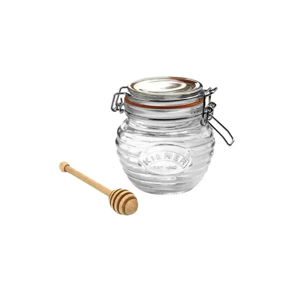 Clear glass jar with a wooden honey dipper on a white background