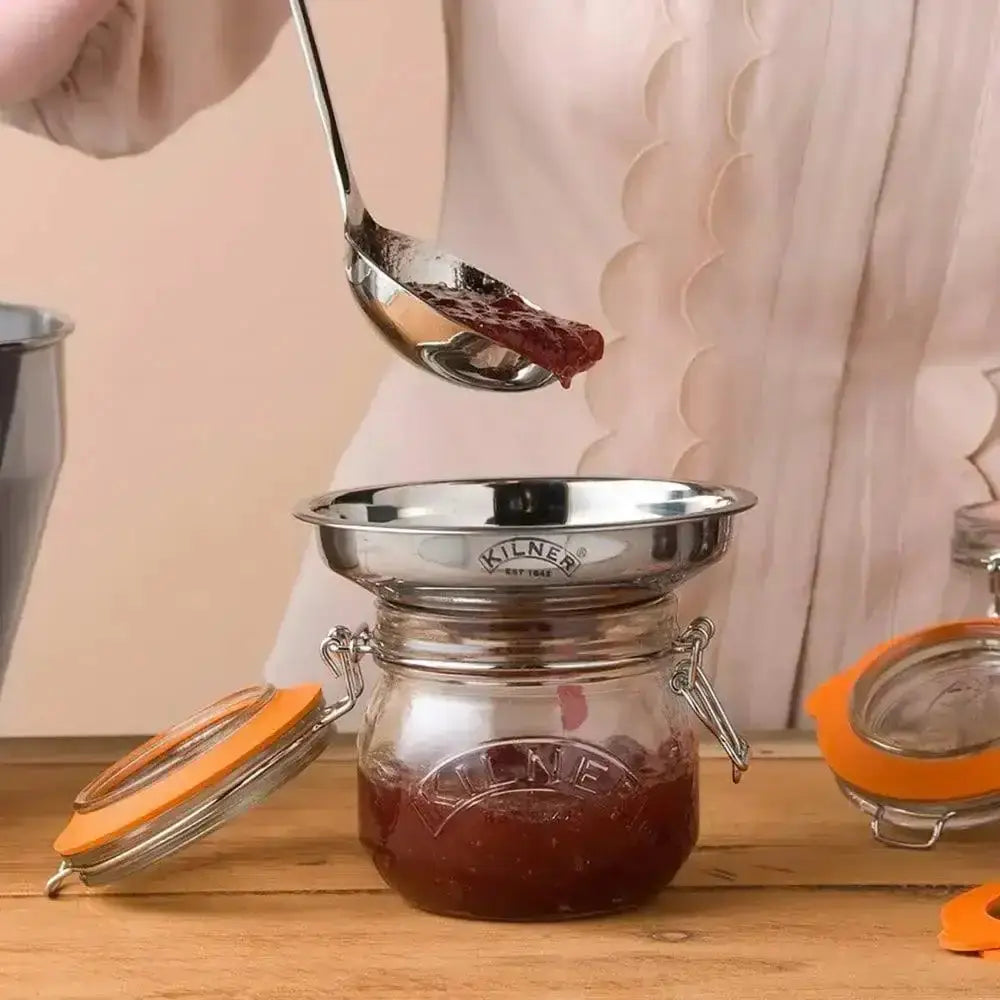 Person using a spoon to scoop jelly from a Kilner jar on a wooden surface.