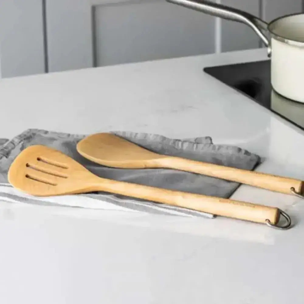 Wooden spatula and spoon on a kitchen counter with a gray towel and pot in the background.