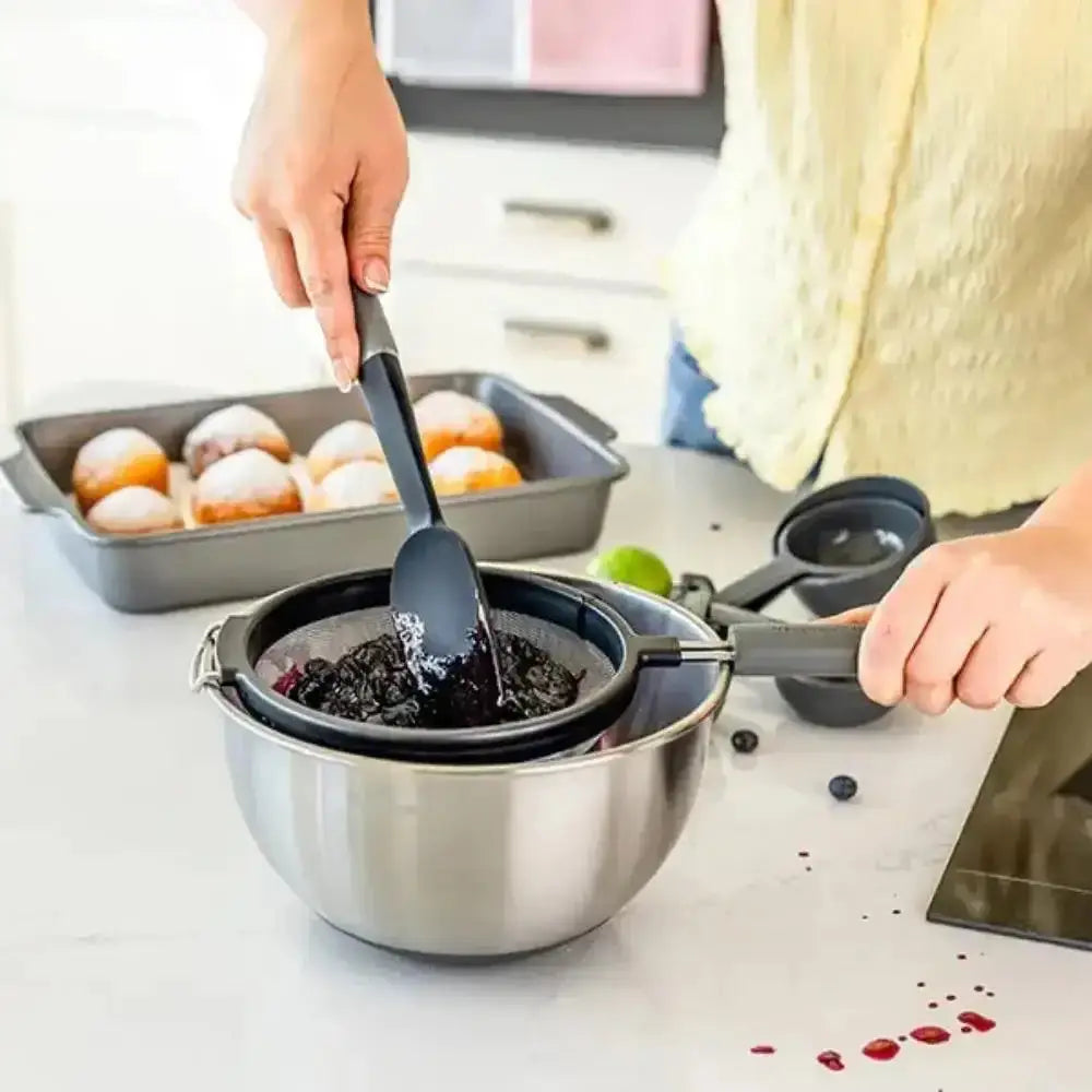 Person using a spatula to transfer food from a pan into a bowl on a kitchen counter.