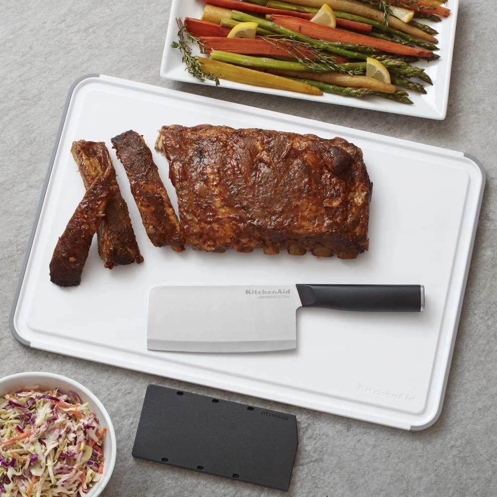 Roasted ribs on a cutting board with a knife, accompanied by vegetables and coleslaw.