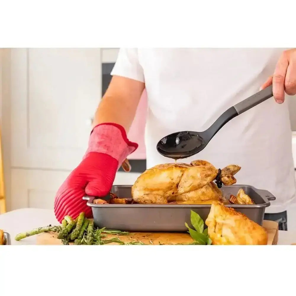Person serving a roasted chicken with a spoon in a kitchen setting