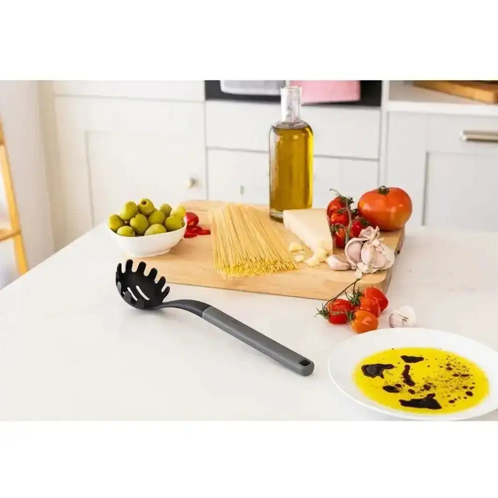 Kitchen counter with pasta, vegetables, and a black ladle on a white countertop.