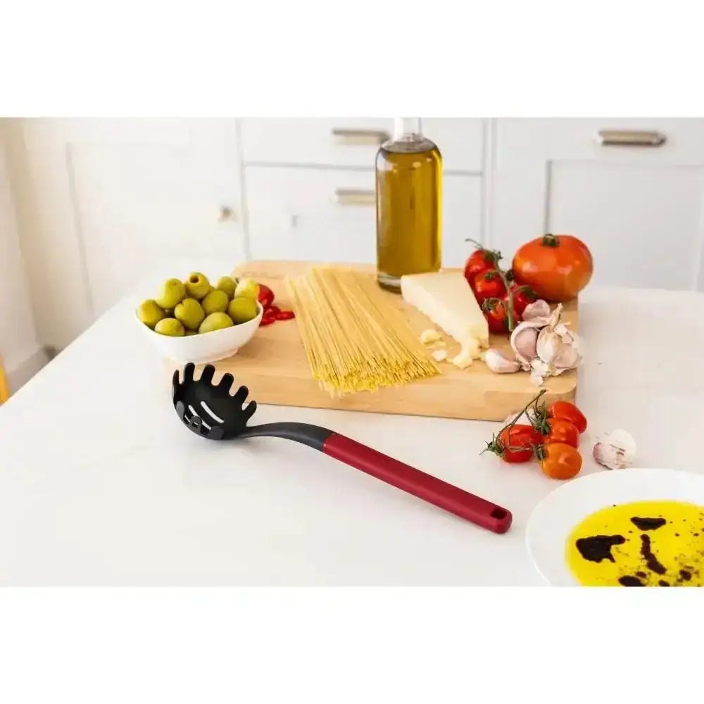 Kitchen counter with pasta, vegetables, and a black slotted spoon on a white countertop.