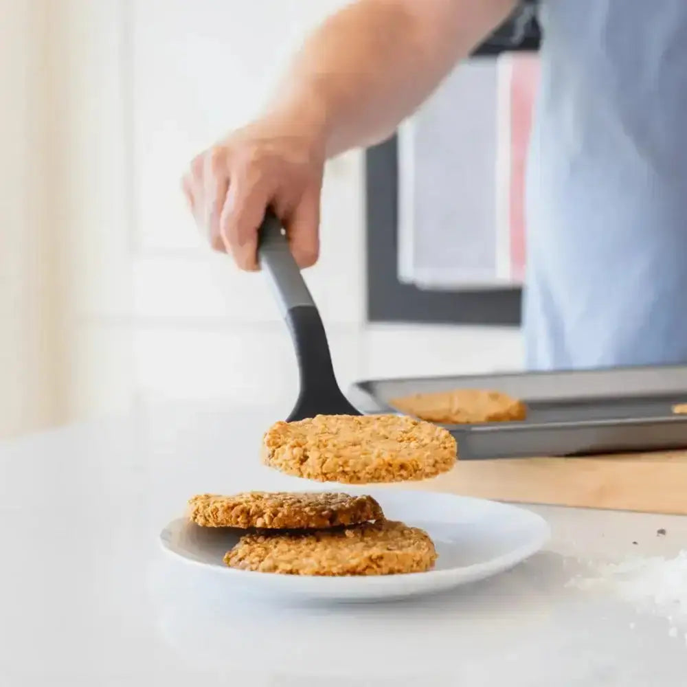 Golden-brown oatmeal cookies being lifted with a grey kitchenaid classic nylon solid turner silicone spatula