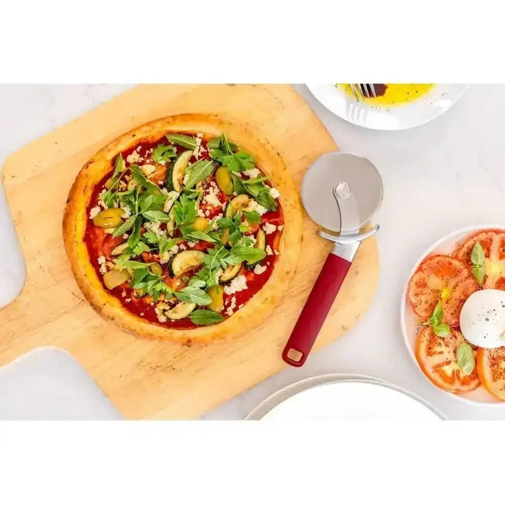 Vegetable pizza on a wooden board with a pizza cutter, served on a white plate.