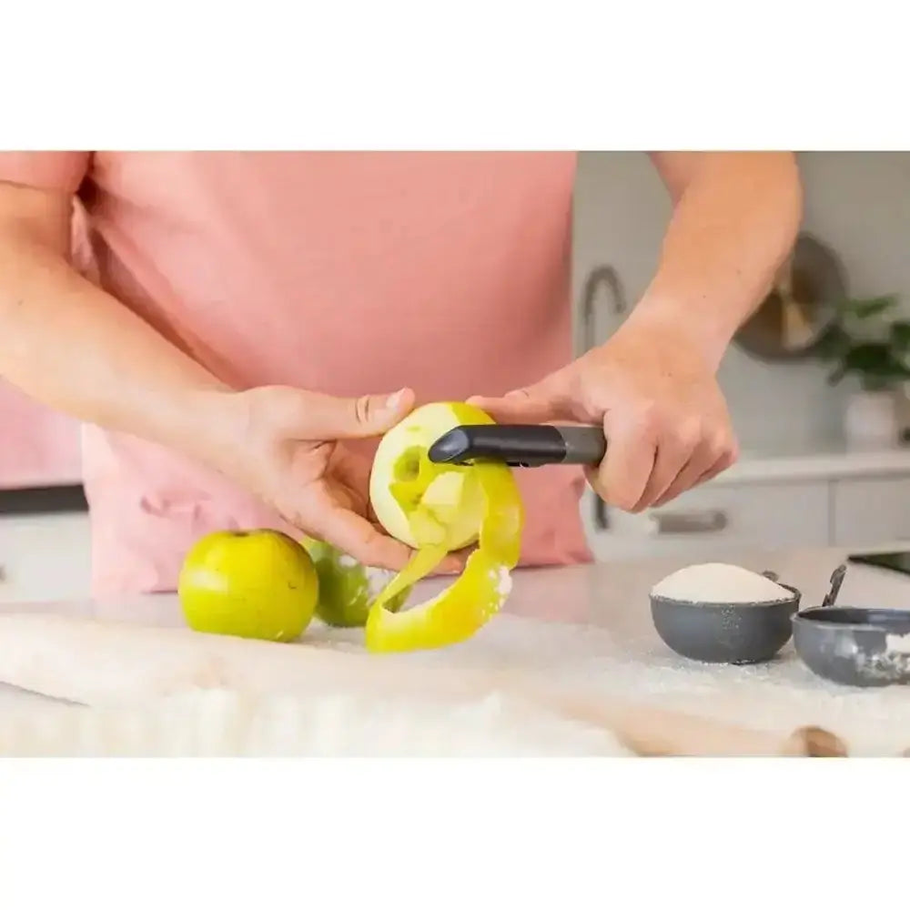 Person using a green apple peeler on a kitchen counter.