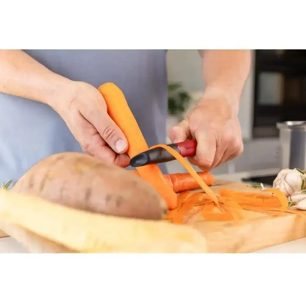 Person using a carrot peeler on a carrot with a blurred kitchen background
