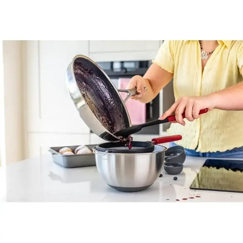 Person using a kitchen tool to transfer food from a pan into a bowl in a kitchen setting.