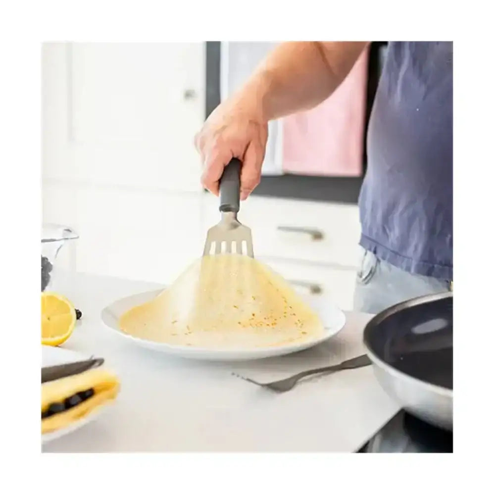 Person using a spatula to serve an omelette onto a plate in a kitchen.