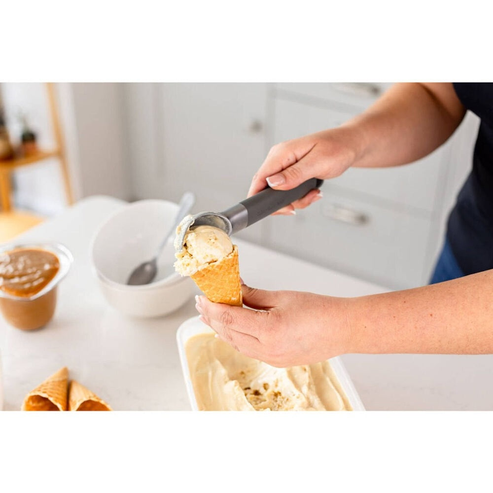 KitchenAid classic stainless steel grey ice cream scoop with black handle serving vanilla ice cream into waffle cone