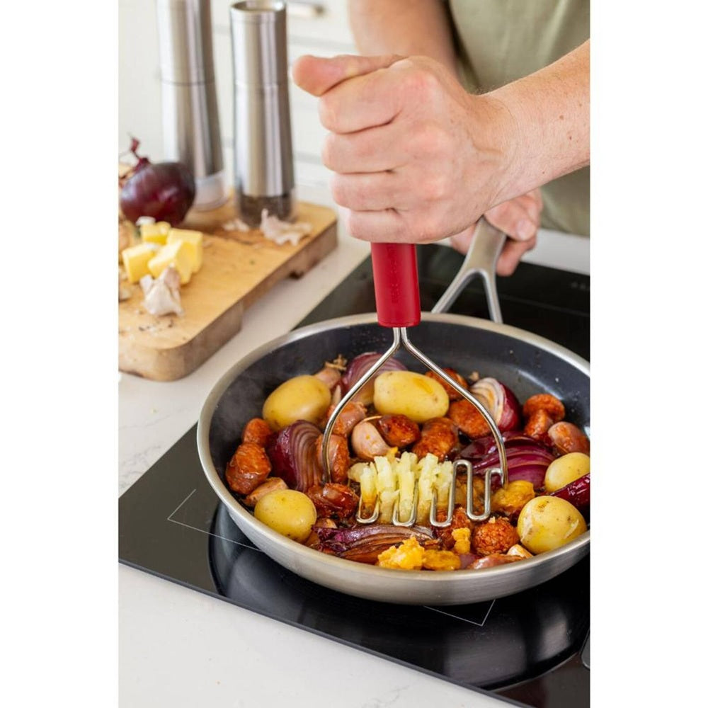 Man mashing a potato in a frying pan with other vegitables with a Stainless Steel wire masher with a red plastic handle on a white background
