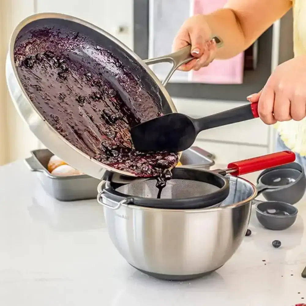 Person pouring a dark liquid from a frying pan into a strainer over a bowl.